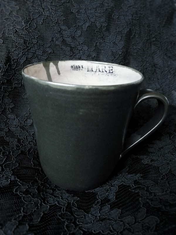 Käsin tehty musta keraaminen muki, jossa stanssattu teksti nightMARE